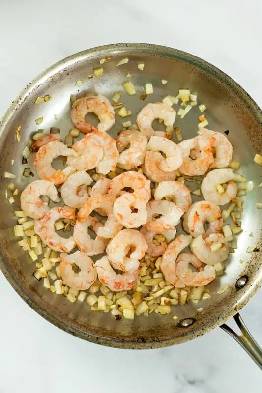Shrimp added to the cooked onion in stainless steel pan.