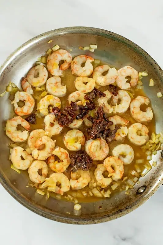 Vegetable broth and sundried tomatoes added to shrimp in pan.