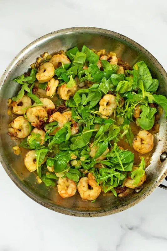 Spinach added to sun dried tomato shrimp in stainless steel pan.