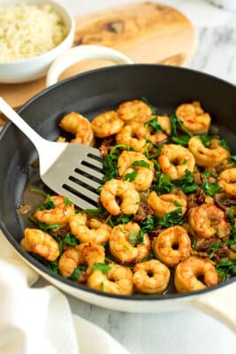 Spatula in a skillet filled with sun dried tomato shirmp.