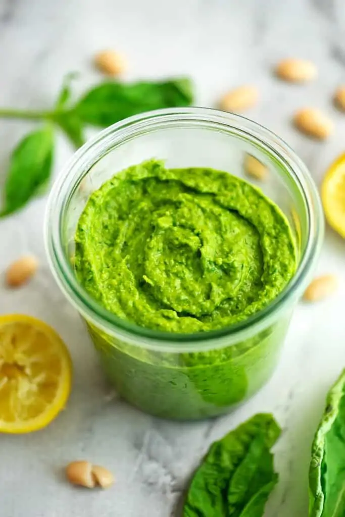 Glass jar filled with white bean pesto, lemons in the background.