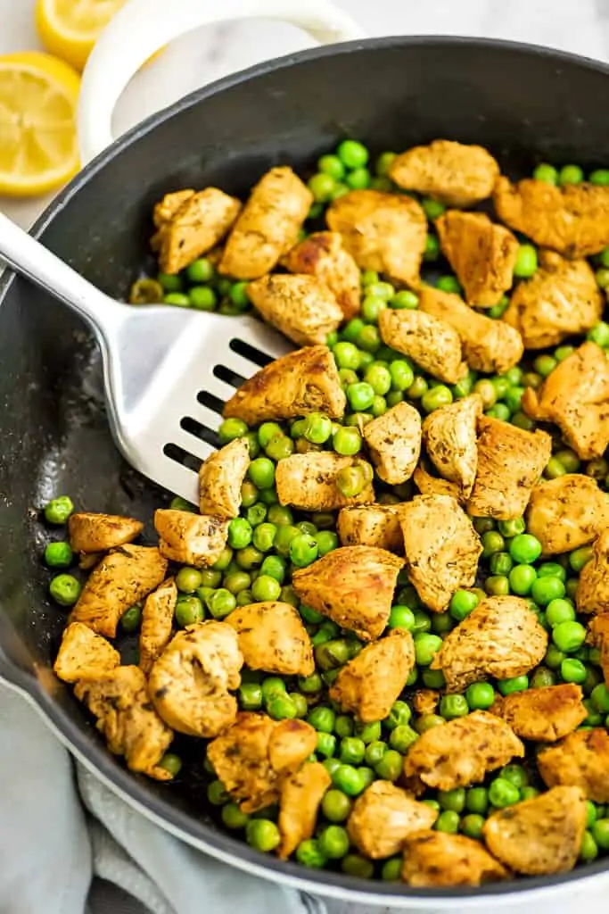Silver spatula in a pan of chicken and peas.