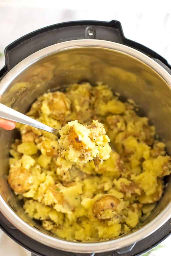 Spoon holding rosemary garlic potatoes over the instant pot.