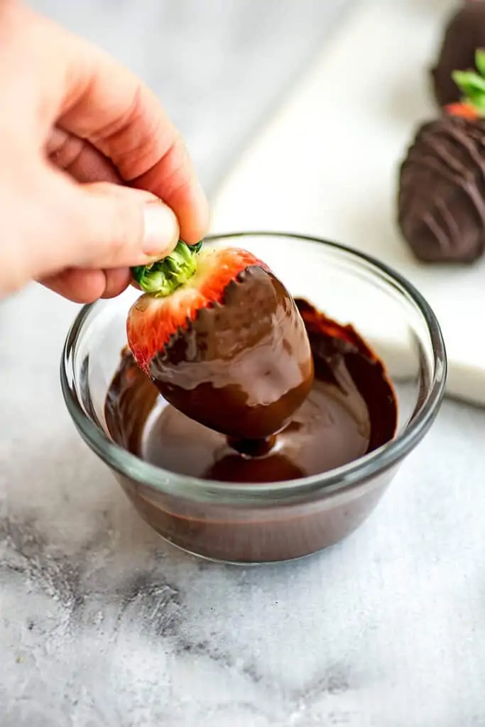 Hand dipping a strawberry in chocolate.