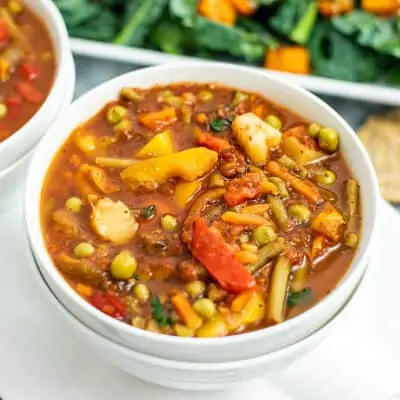 Bowl of vegetable soup with salad in background.