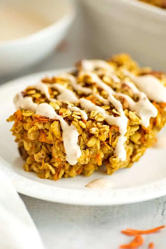 Baked carrot cake oatmeal on a plate with maple frosting drizzle.