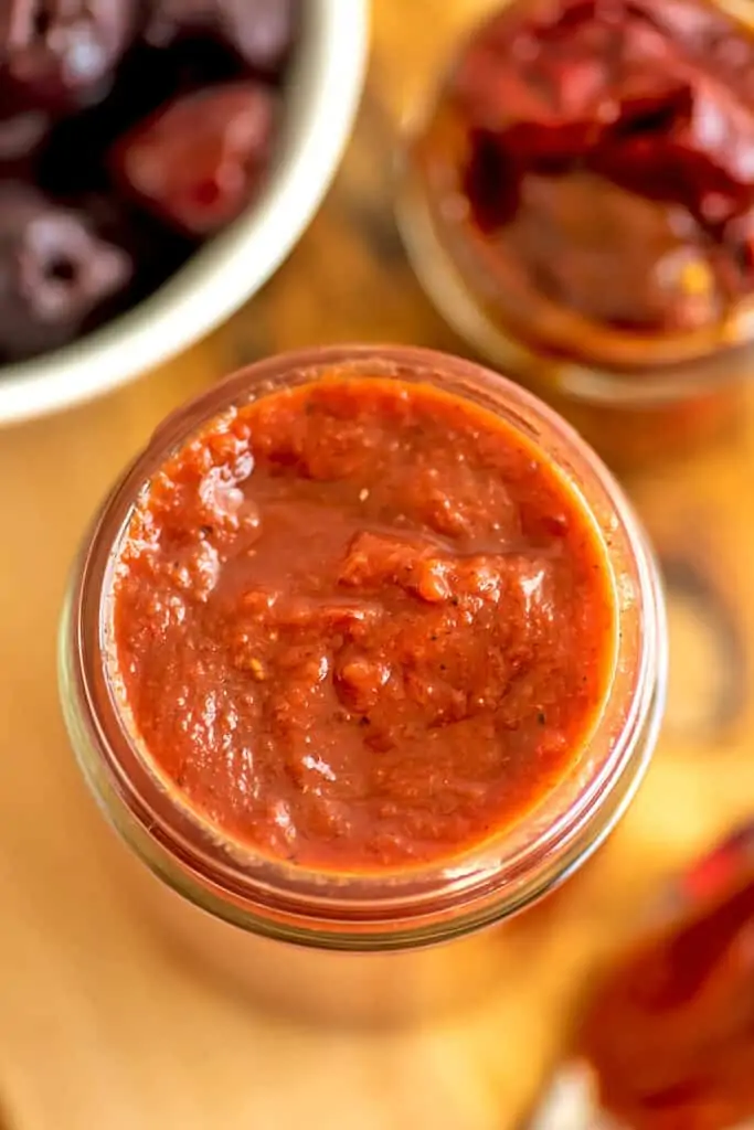 Chipotle cherry bbq sauce in a glass jar with chipotles in background.