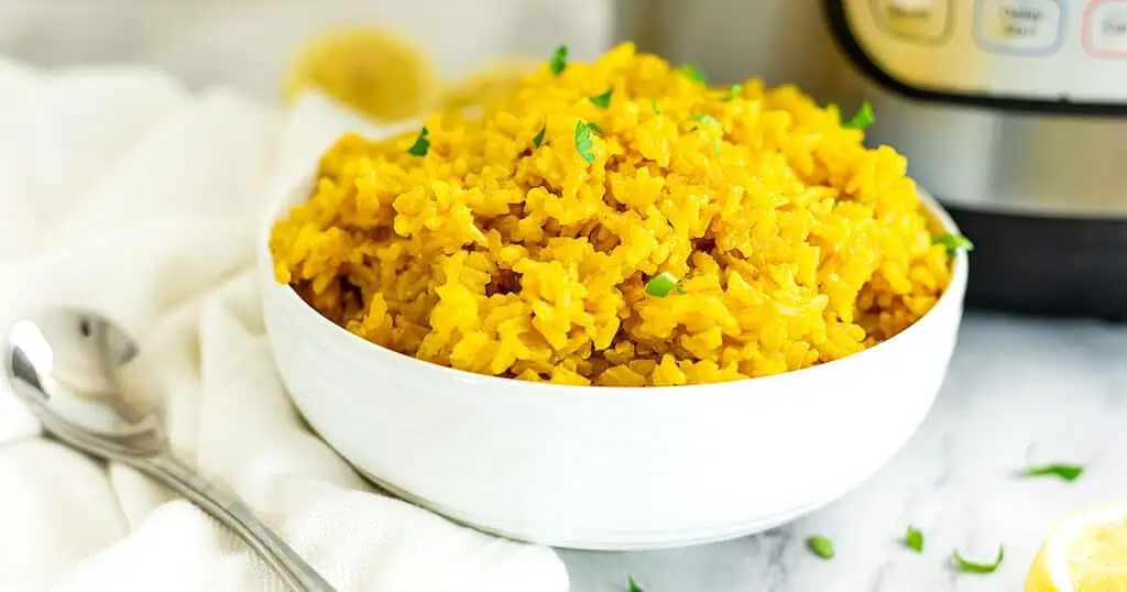 White bowl filled with yellow rice, instant pot in background.