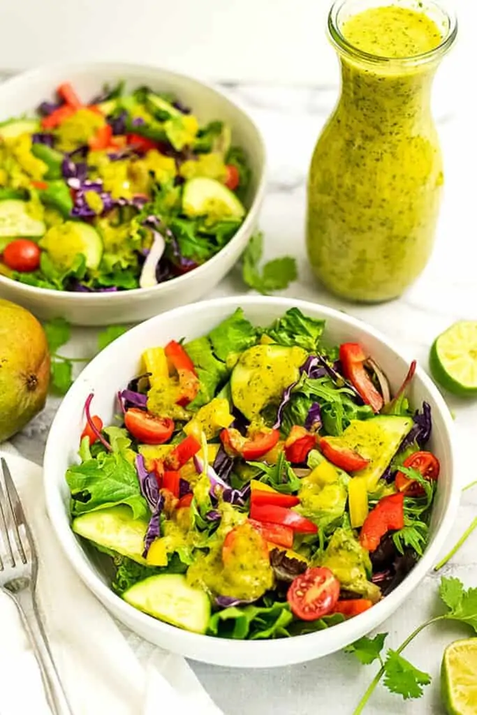 Salad in white bowl with mango dressing drizzled on top.