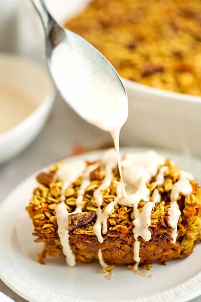 Spoon drizzling frosting over baked carrot cake oatmeal.