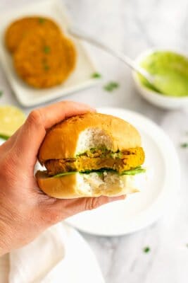 Hand holding a sweet potato lentil burger with a bite taken.