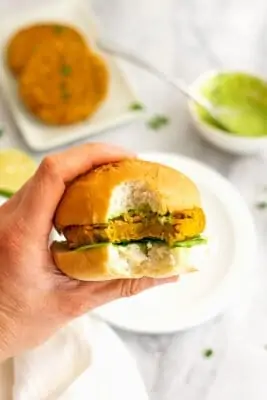 Hand holding a sweet potato lentil burger with a bite taken.