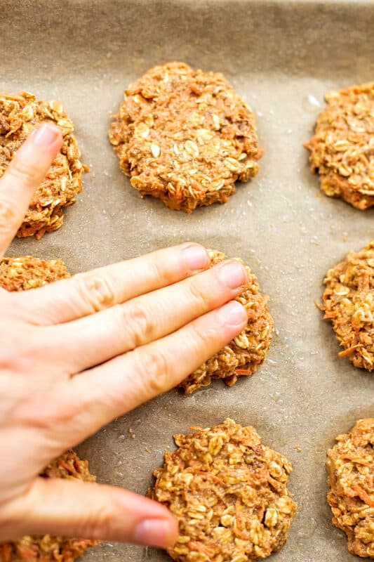 Hand pressing down on carrot cake cookies to flatten them.