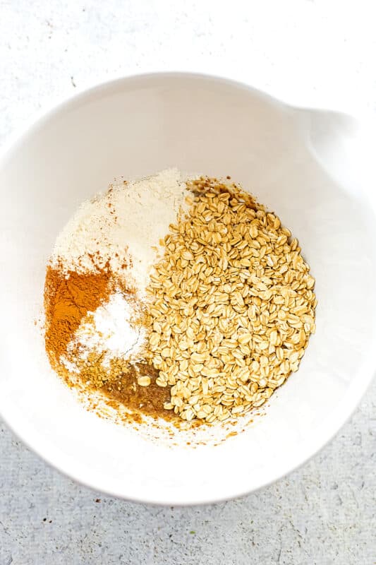 Rolled oats, flour, spices added to large white bowl with flax.