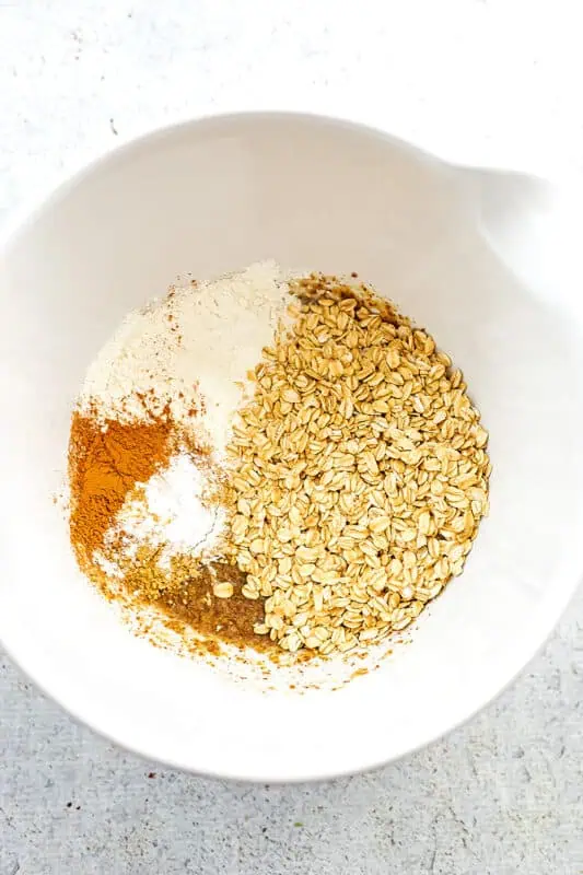 Rolled oats, flour, spices added to large white bowl with flax.