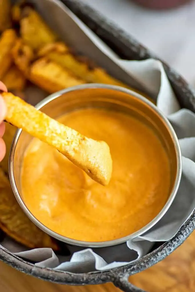 Fry being dipped in vegan chipotle sauce.