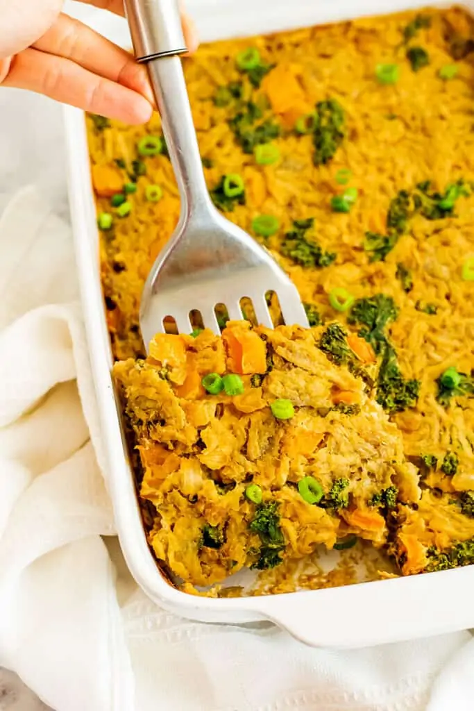 Vegan hash brown casserole being served with a silver spatula.