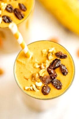 Carrot banana smoothie in a glass topped with raisins and walnuts.