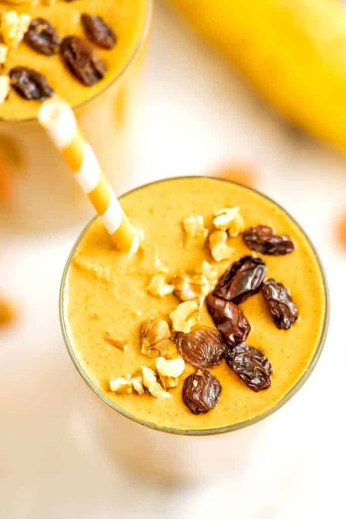 Carrot banana smoothie in a glass topped with raisins and walnuts. 