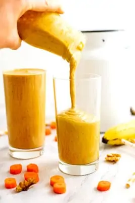 Bottle pouring carrot banana smoothie in a glass.
