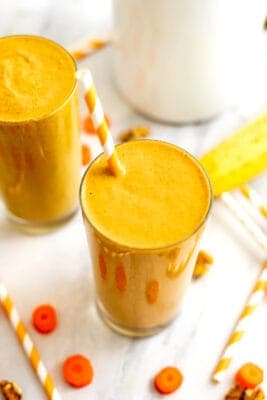Carrot banana smoothie in a glass with orange straw.