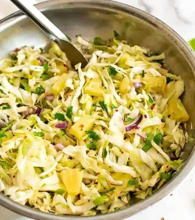 Large silver bowl filled with pineapple slaw with tongs.