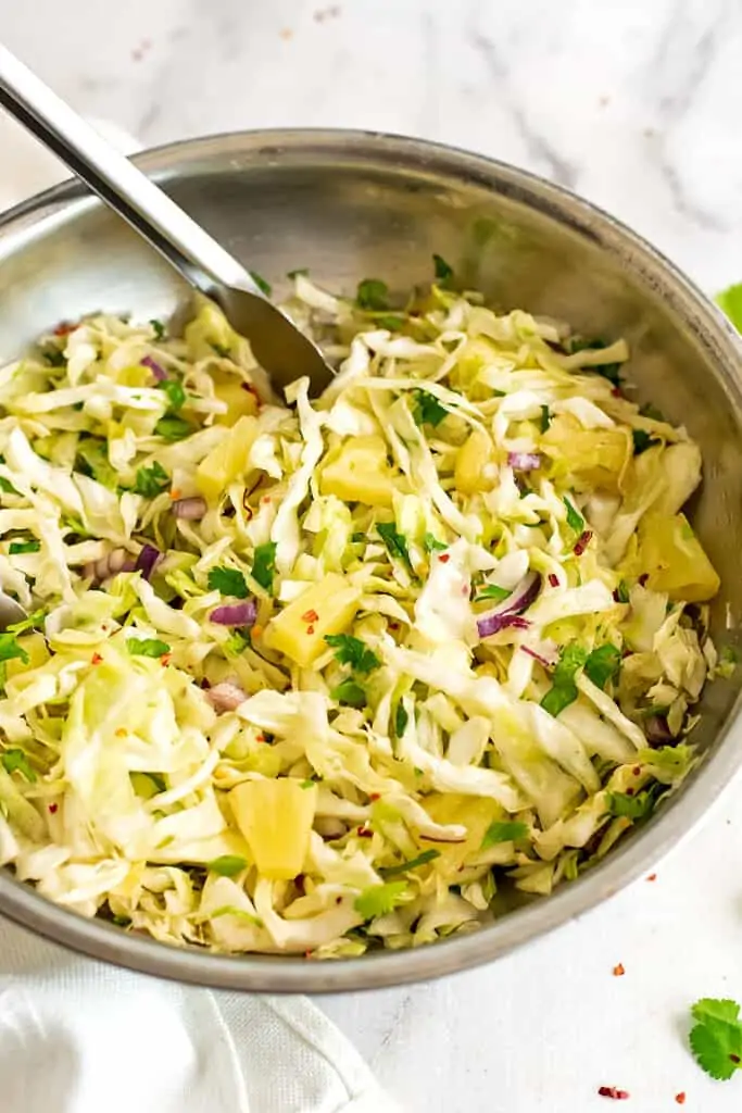 Large silver bowl filled with pineapple slaw with tongs.
