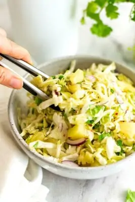 Tongs getting a serving of pineapple coleslaw (no mayo).