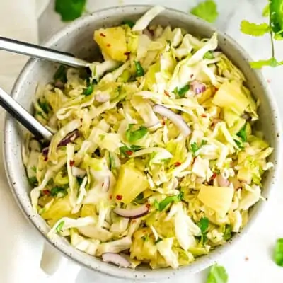 Pineapple coleslaw in a large bowl with tongs.