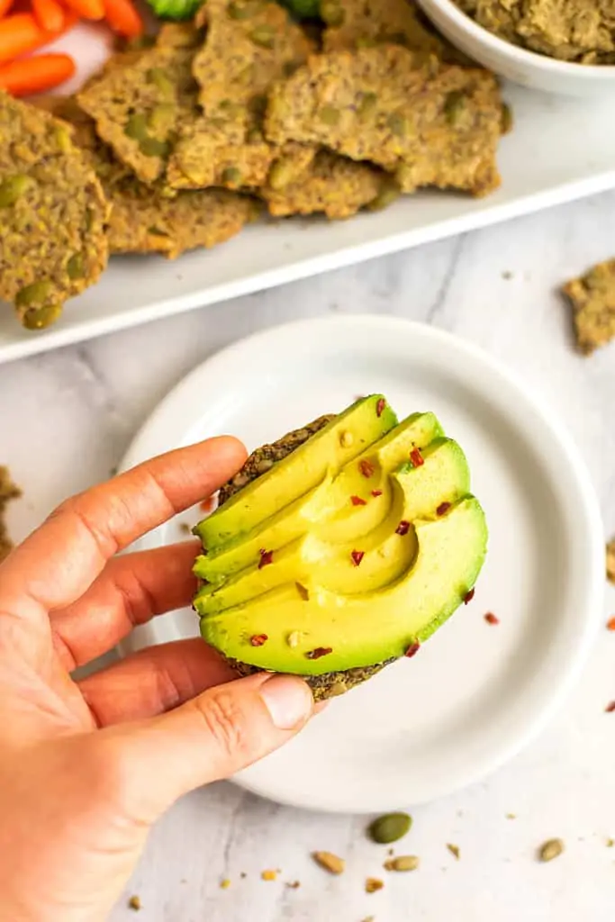 Avocado slices on a seed cracker over a plate.