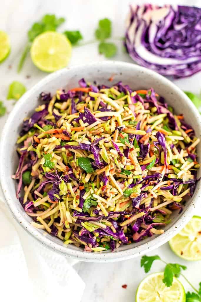 Large bowl of sesame ginger broccoli slaw with cabbage in background.