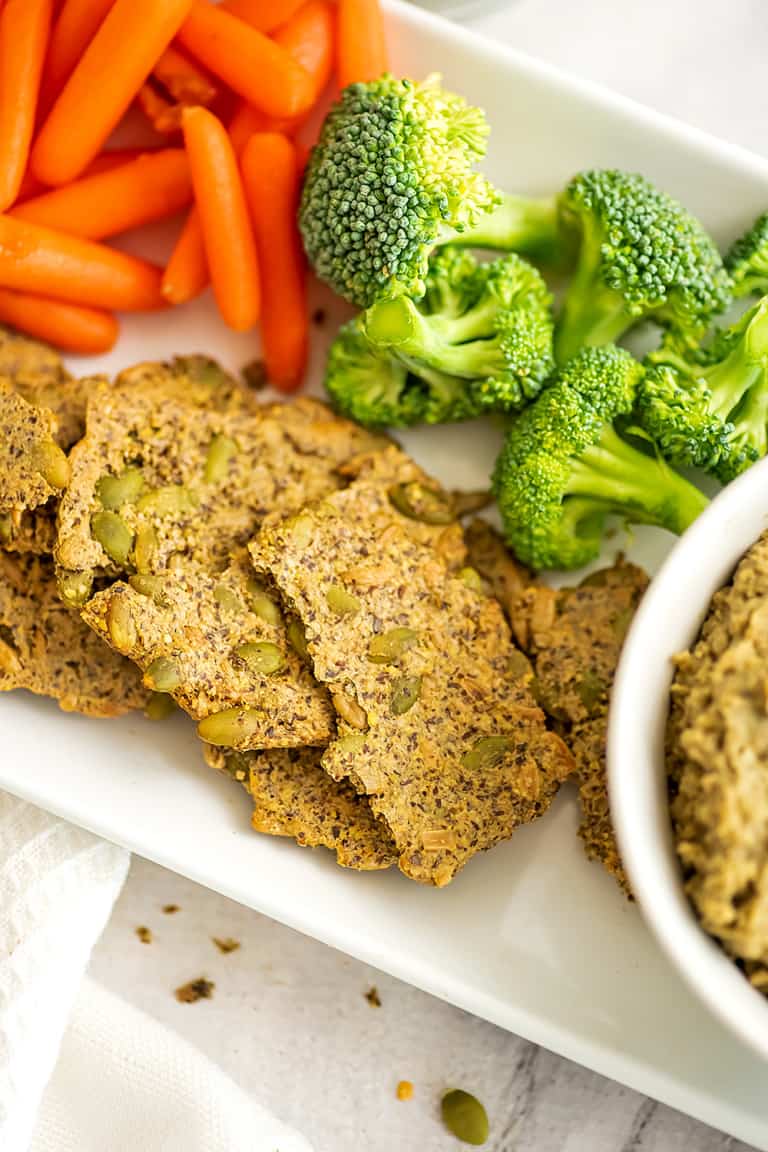 Serving dish with carrots, broccoli and seed crackers.