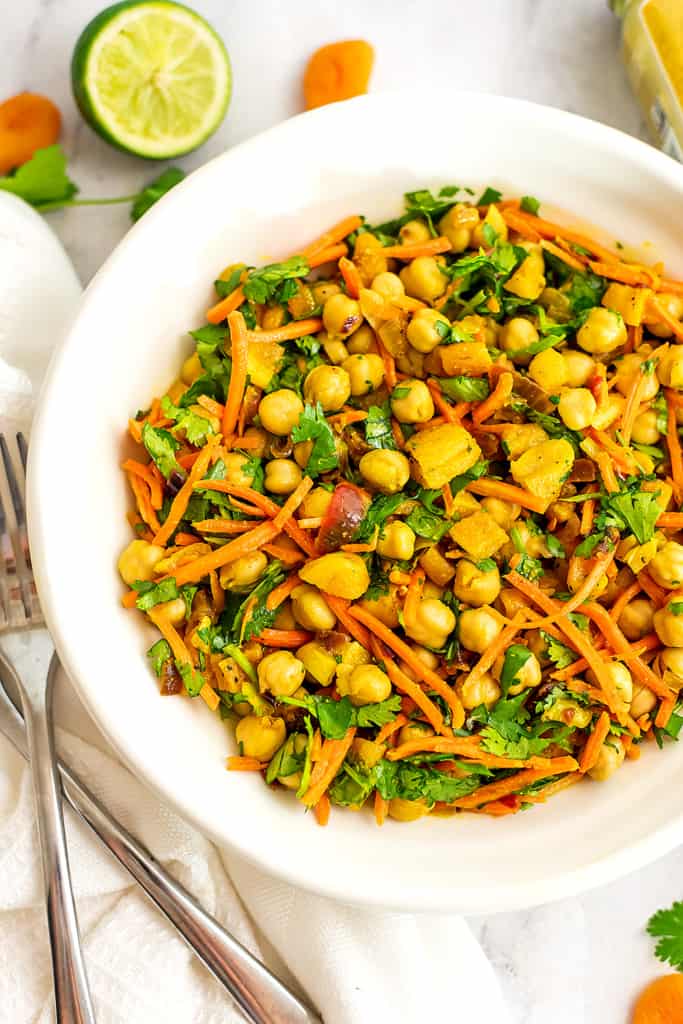 Apricot chickpea curry in large bowl with limes in background.