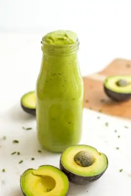 Bottle of vegan avocado dressing with avocados in background..