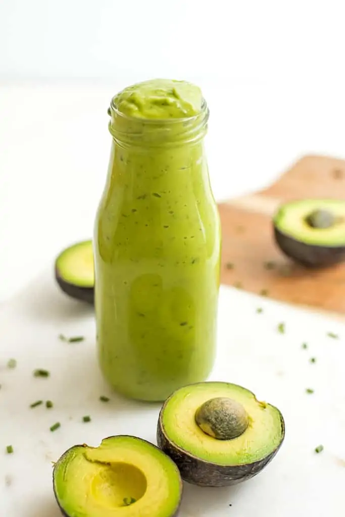 Bottle of vegan avocado dressing with avocados in background..