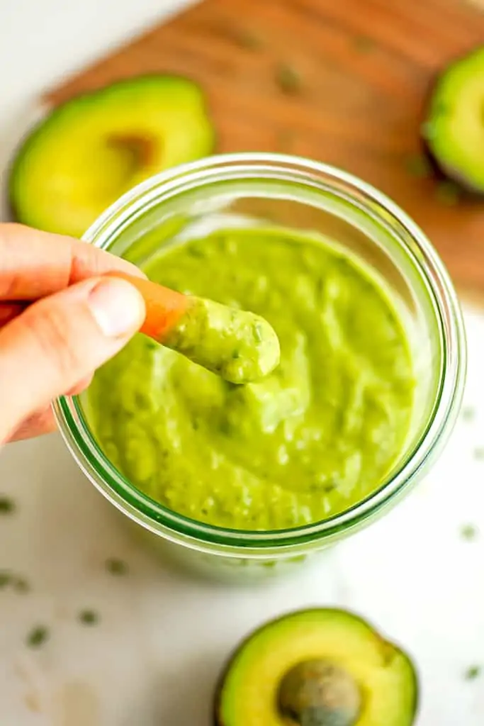 Carrot being dipped in avocado ranch dressing.