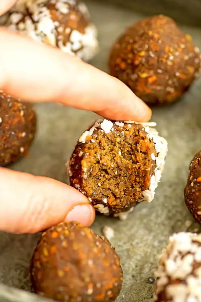 Hand reaching for a single carrot cake protein ball with bite taken from it.