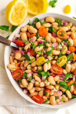 Greek white bean salad in serving bowl with wooden spoon.