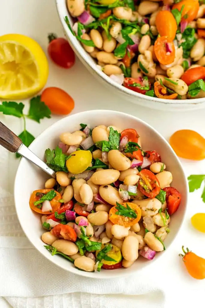 Small white bowl filled with greek white bean salad and a spoon.
