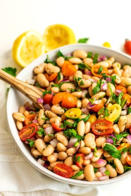 Serving dish filled with greek white bean salad and wooden spoon.