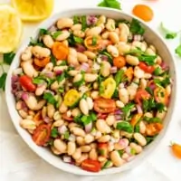 Greek white bean salad in a bowl with lemons in background.