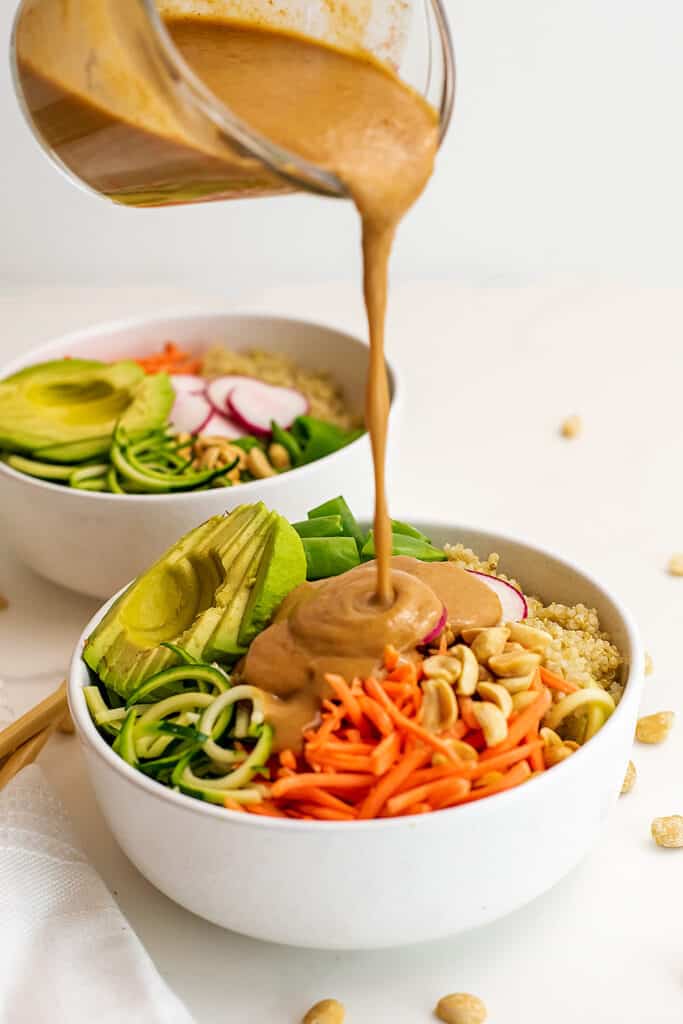 Peanut dressing being poured over asian zoodle bowl.