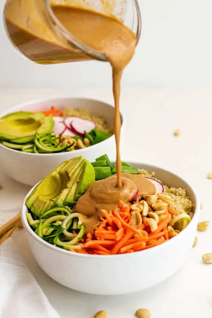 Peanut dressing being poured over asian zoodle bowl.