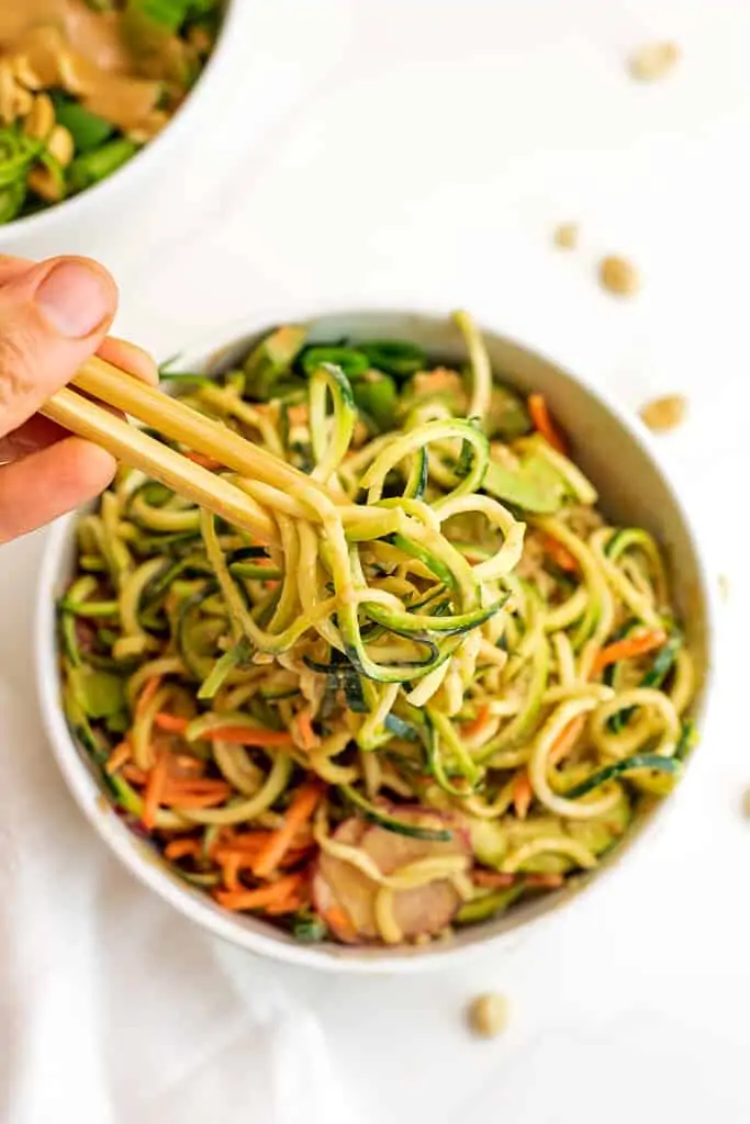 Chopsticks grabbing zucchini noodles from a zoodle bowl.
