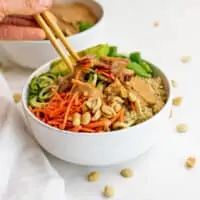 Chopsticks in a bowl filled with zucchini noodles and peanut dressing.