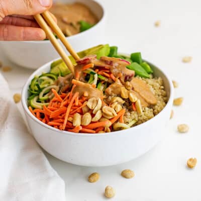 Chopsticks in a bowl filled with zucchini noodles and peanut dressing.