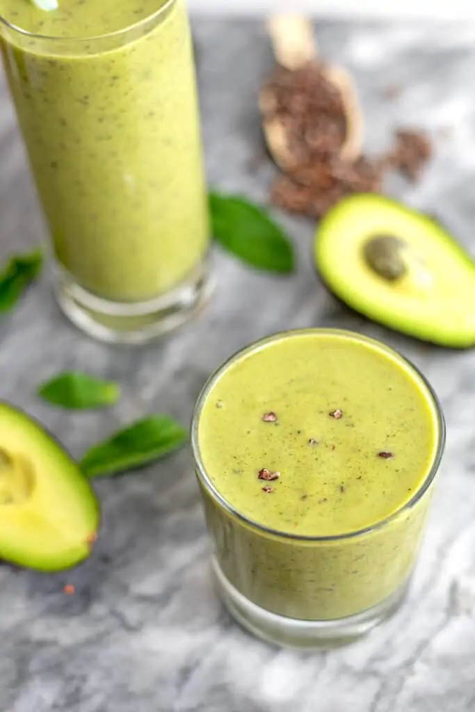 Short glass filled with mint protein shake with avocado in background. 