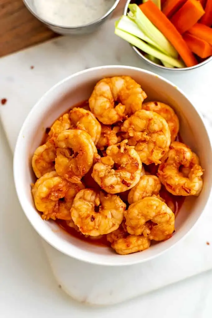 Grilled buffalo shrimp with celery and carrots in background.