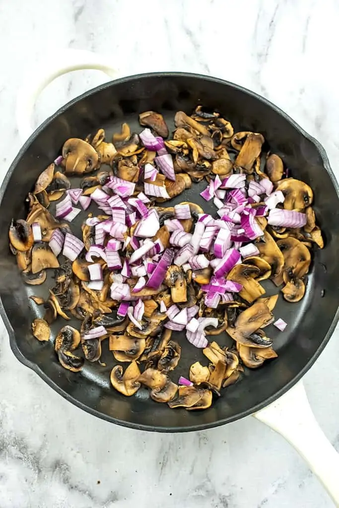 Cooked mushrooms and red onions in a skillet.
