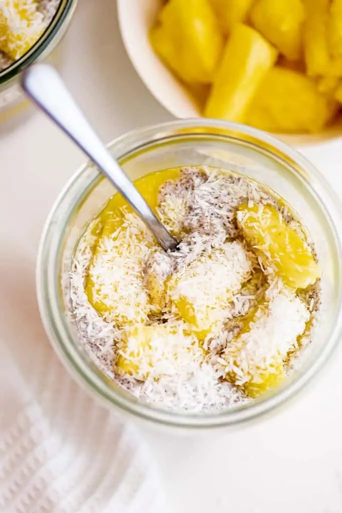 Glass jar full of chia pudding with pineapples and coconut on top.